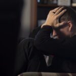 um homem sentado em um sofá segurando a cabeça em suas mãos