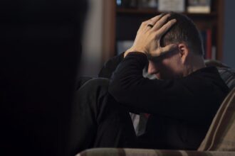 um homem sentado em um sofá segurando a cabeça em suas mãos