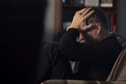 um homem sentado em um sofá segurando a cabeça em suas mãos