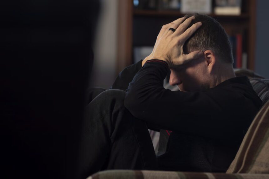 um homem sentado em um sofá segurando a cabeça em suas mãos