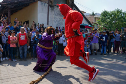 Ator fantaseado de Jesus segurando um crucifixo e apontando para o outro ator, fantasiado de Diabo.
